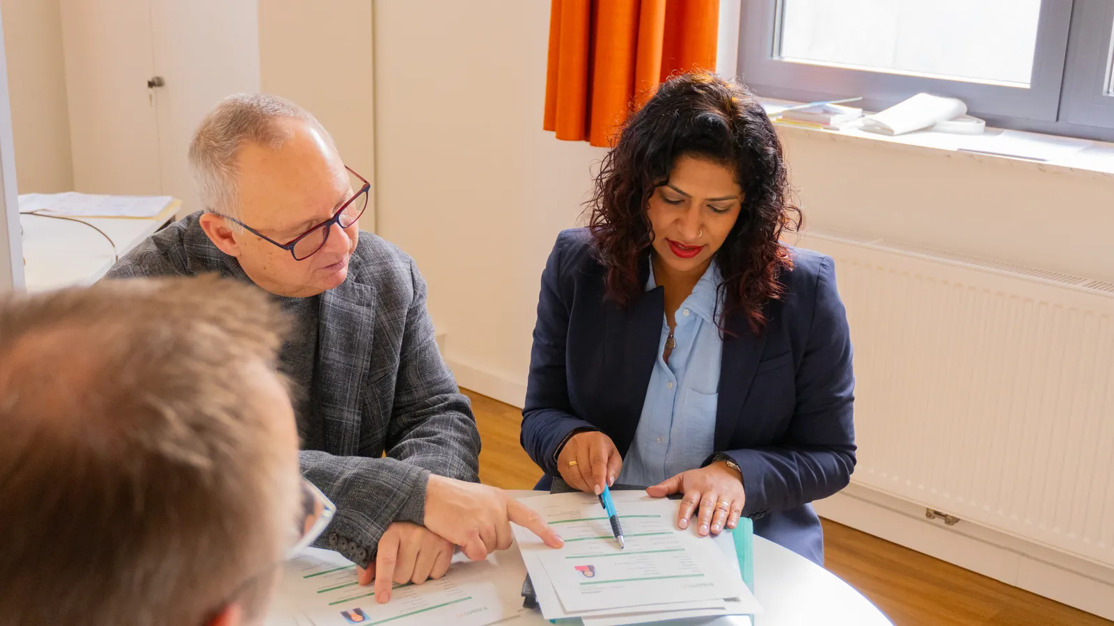 Baicy Terbrüggen geht in einem Beratungsgespräch am Tisch Unterlagen mit ihrem Gegenüber durch
